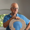 A smiling man holds the wooden frame of a cello.