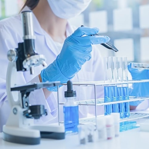  Scientist handling test tubes filled with blue liquid beside a microscope and other laboratory equipment