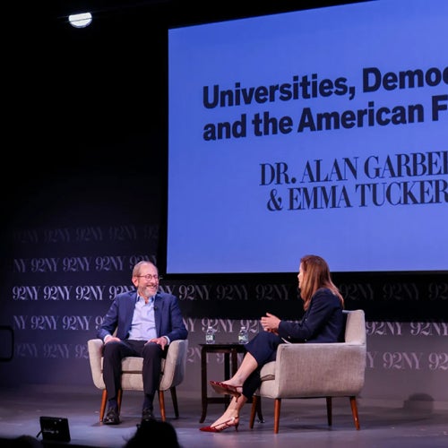President Garber and Emma Tucker sit on stage with Universities, Democracy, and the American Future sign behind them.