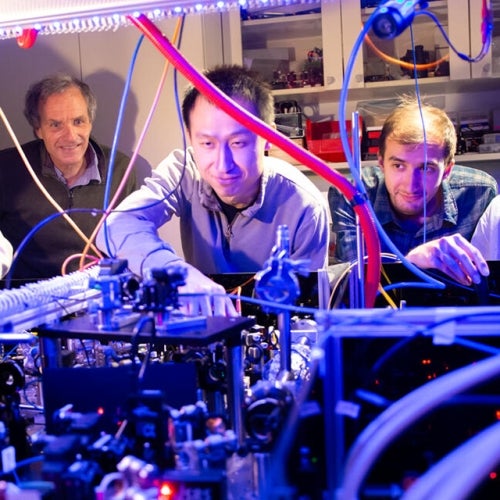Researchers work together around a complex lab experiment with wires and optical equipment.