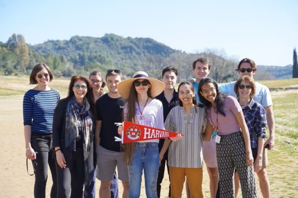 Professor Naomi Weiss and travelers posing with Harvard pennant in Olympia