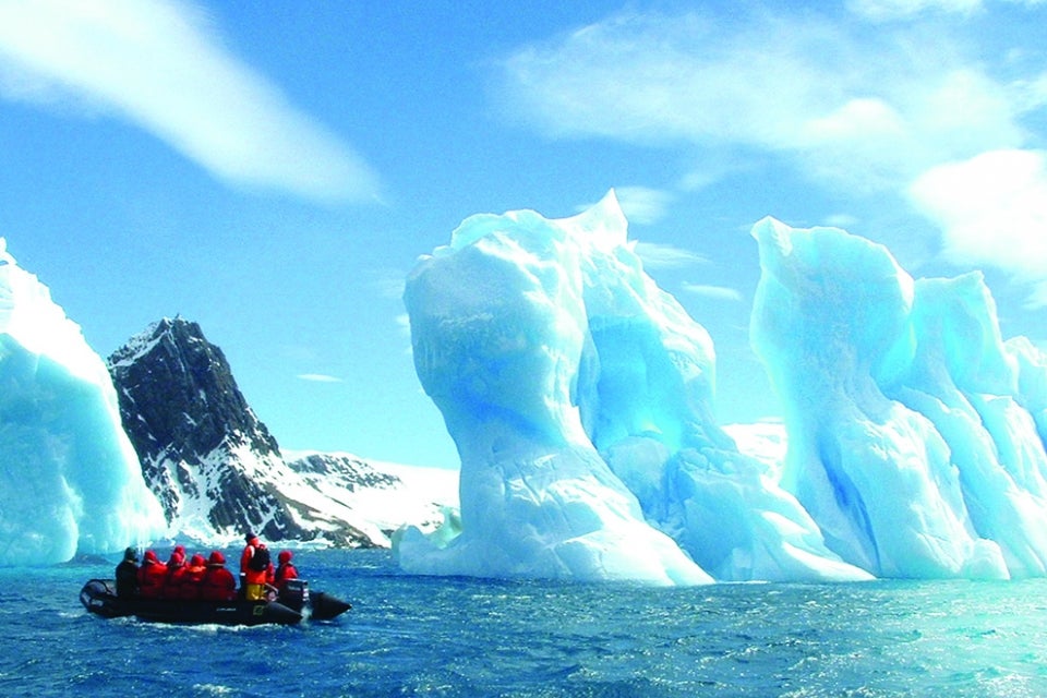 people on zodiac boat near iceberg